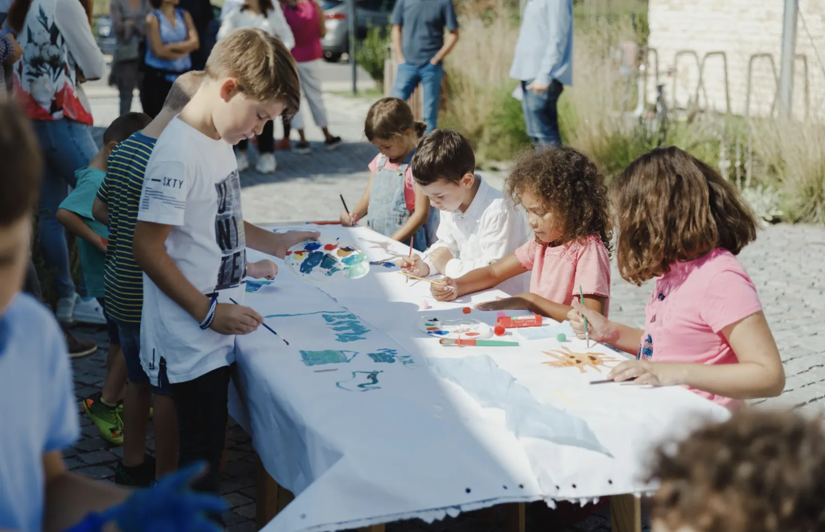 Crianças pintando juntas em uma mesa comprida ao ar livre